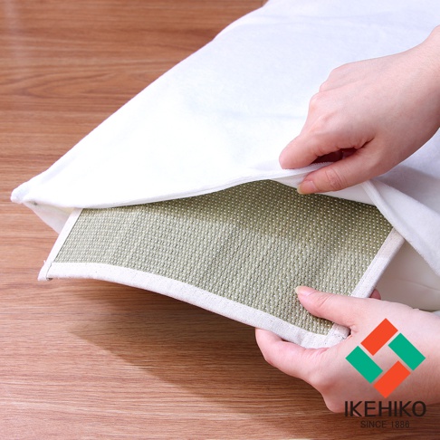 一雙手正在將一個淺綠色的藺草編織枕墊塞入白色的枕頭套中，枕墊表面有細小的白色網點，邊緣有米白色的包邊。