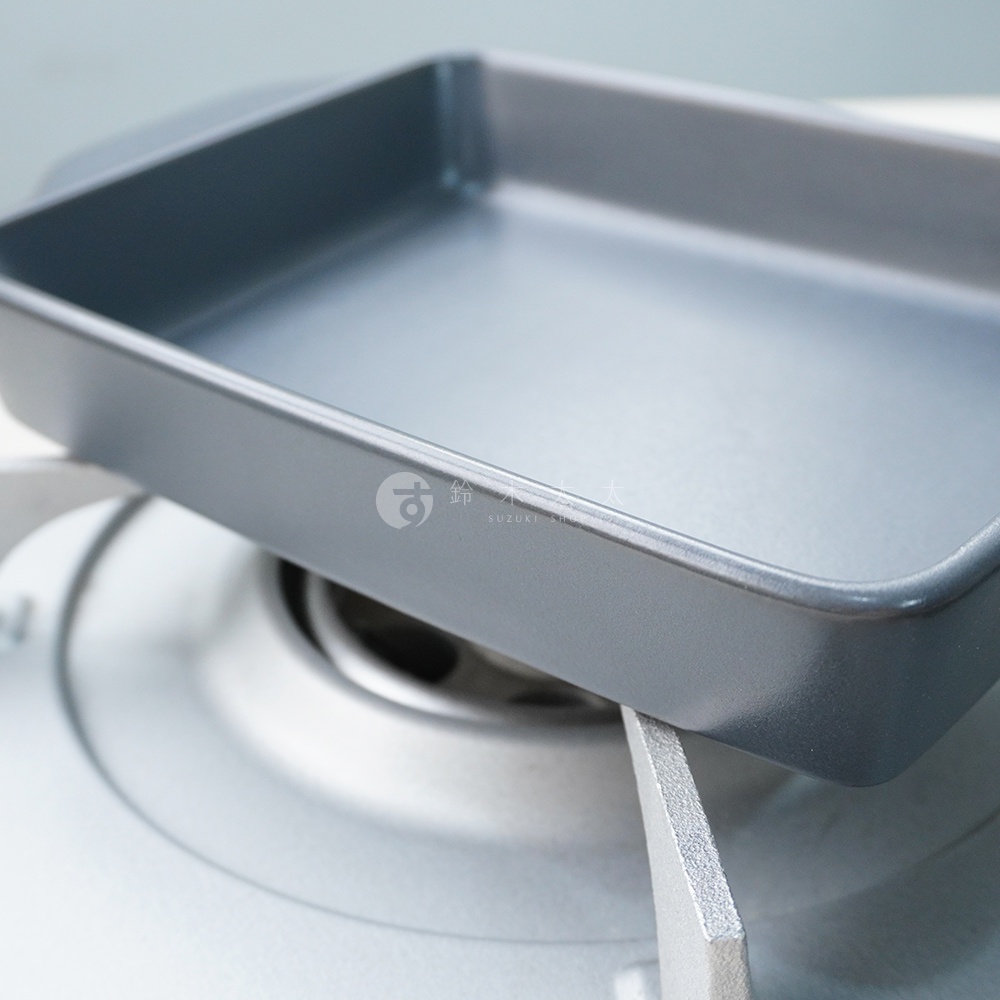 一個平底的灰色耐熱陶製烤盤，邊緣有輕微的圓角，放在爐架上。