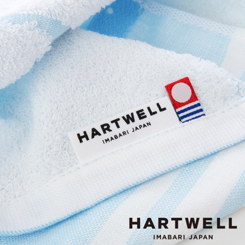 今治純棉條紋紗布毛巾，以白色為底，搭配淺藍色條紋。毛巾柔軟，帶有品牌標籤「HARTWELL IMABARI JAPAN」及日式圖案小標籤。