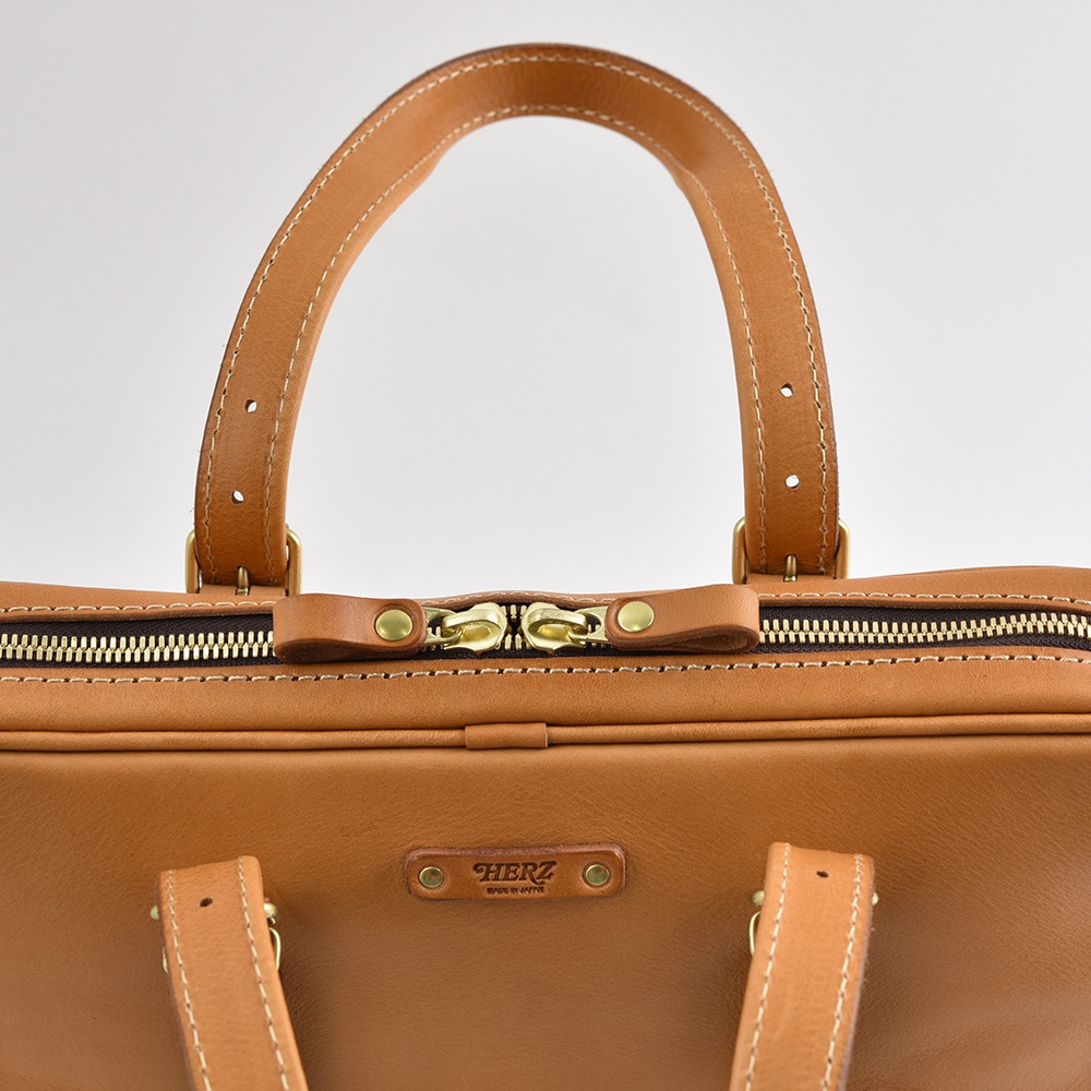 棕色皮革製成的公事包，有兩條手提把、金色拉鍊與品牌標誌。