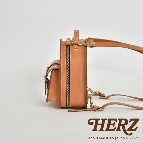 職人手作皮革迷你後背包，展示側邊視角，皮革顏色為棕褐色，搭配黃銅色拉鍊與扣環，結構紮實，設計簡約。
