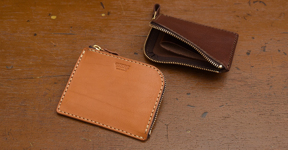 皮革L型拉鍊迷你短夾，近景為淺棕色皮革，壓印有品牌標誌；遠景為深棕色皮革，拉鍊部分敞開，露出內部。兩者皆為手作皮革製品。