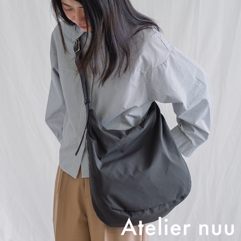 Atelier nuu 品牌，一位女性身穿條紋襯衫和卡其色長褲，肩上斜背一個深灰色布質托特包。