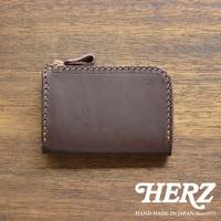 深棕色皮革製的短夾，配有金色拉鍊和同色皮革拉環，邊緣以咖啡色縫線裝飾，整體放在木紋桌面。