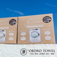 兩件式卡其色環保永續毛巾包裝盒，上面印有日文說明與洗衣機圖示，強調節電節水與尺寸規格。