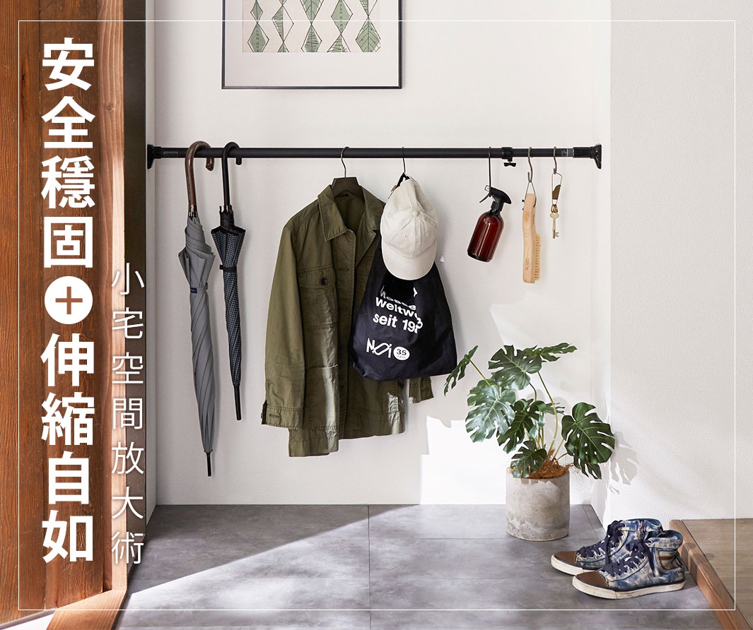 黑桿全功能伸縮置物架，掛有兩把傘、一件軍綠色外套、一頂白色帽子、一個黑色環保袋、一個棕色噴瓶、木質衣刷、鑰匙和一盆綠葉植物。