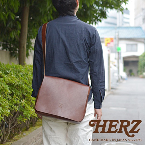 一位身穿深藍色襯衫、米白色長褲的男子，背著一個棕色皮革斜背包，包包上印有「Z」字樣。