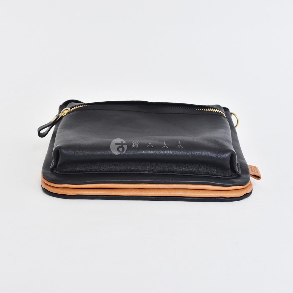 黑色皮革翻轉雙色直式斜背包，包身下方有淺棕色皮革層疊，金色拉鍊，一個皮革拉袢。