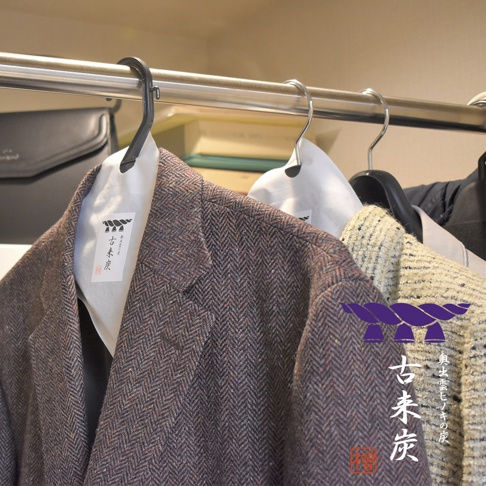 兩件斜紋軟呢夾克掛在衣架上，其中一件夾克有標示「古來炭」字樣的白色調濕紙，另件夾克則有紫色繩結圖案和「古來炭」日文標示。