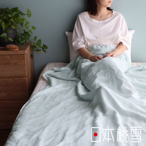 一位女性坐在床上，蓋著一條淺綠色的二層紗半毯。毯子材質輕柔，呈現絲滑的質感。