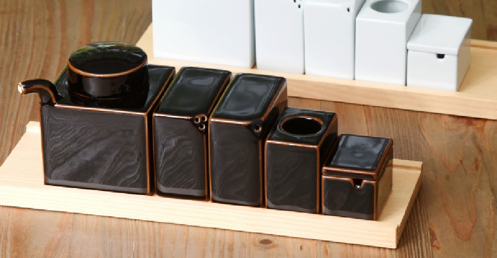 黑色調味五件組，包含帶有金屬邊緣的醬油瓶、三個方形調味罐及一個小方盒，皆擺放在淺色木質托盤上。