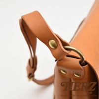 日本HERZ品牌皮革雙扣旅行郵差包近拍，展示金屬環和皮帶連接處的細節，背景為白色。