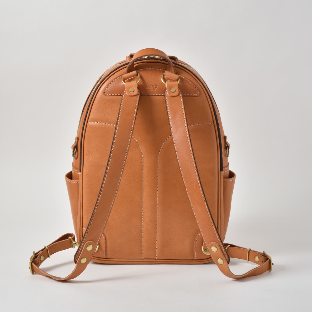 職人手作皮革多功能後背包 R-21，採用天然皮革材質，呈現溫潤的棕褐色調。雙肩帶設計，可調節長度，配有側邊口袋及精緻車縫線，整體簡約實用。