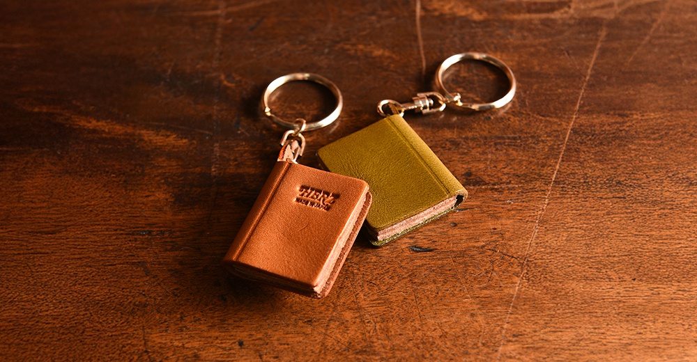 兩個皮革書本造型鑰匙圈，一個為棕褐色，印有「HERZ MADE IN JAPAN」字樣；另一個為橄欖綠色。