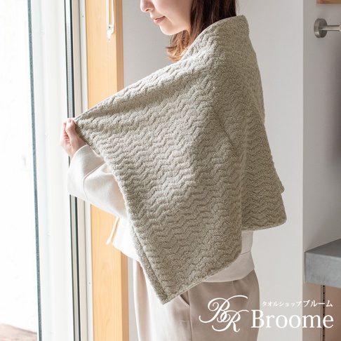 Broome 品牌一款灰綠色緹花織法迷你浴巾，細緻波浪圖案，由一位女士披在肩上，展示其柔軟質感。