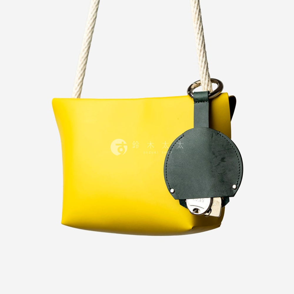 黃色方形皮革包，搭配深綠色皮革圓形鑰匙包，內含鑰匙，並附有繩索背帶。
