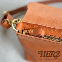 HERZ 職人手作皮革斜背包，金屬拉鍊和黃銅扣環細節，呈現手工質感。