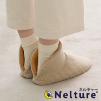 一雙米色菱格紋布面、黃色內襯的保暖腳踝室內拖鞋，由穿著米色寬褲和米色襪子的人穿著，置於淺灰色地毯上。