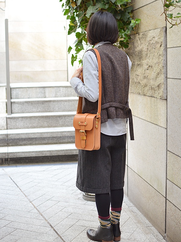 棕褐色皮革製成、帶有金屬皮扣的單肩包，由一位女士背在肩上。