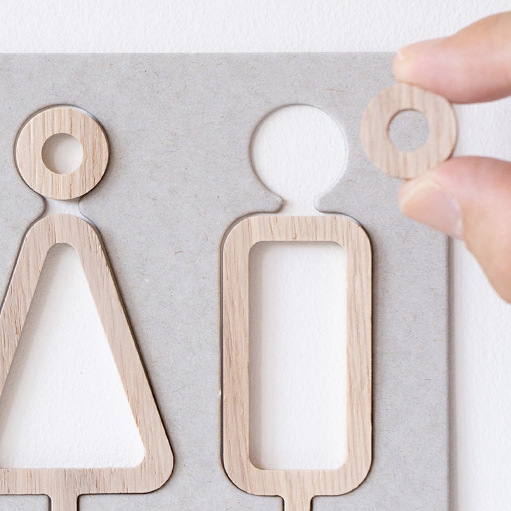 淺灰色底板上的木製男女標示牌，分別以三角形和方形代表，上面有圓形頭部設計。