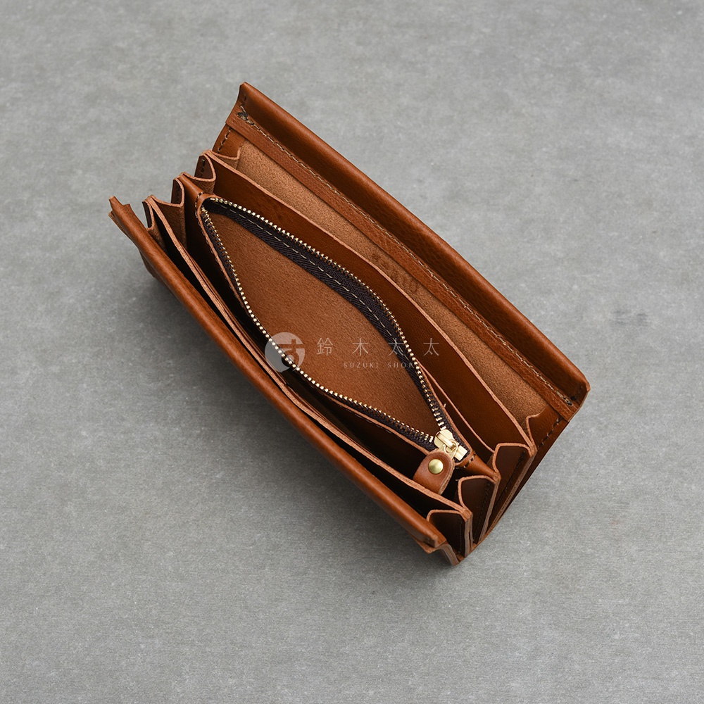 這是一個採用棕色皮革材質製作的長夾，呈現半開啟狀態。內部設計有多層次隔間與一個拉鍊式零錢袋，整體外型簡潔精緻，皮革紋理自然，並在內部印有鈴木商店的品牌標誌。
