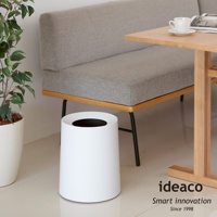 簡約白色圓形家用垃圾桶，上方有黑色開口，置於灰色沙發和木桌旁。