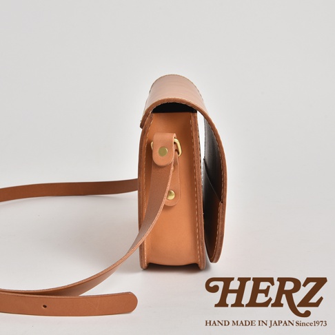 職人手作皮革翻蓋橫式單肩包，呈現自然原色皮革紋理，配有可調節長度的皮革肩帶及金屬釦件。