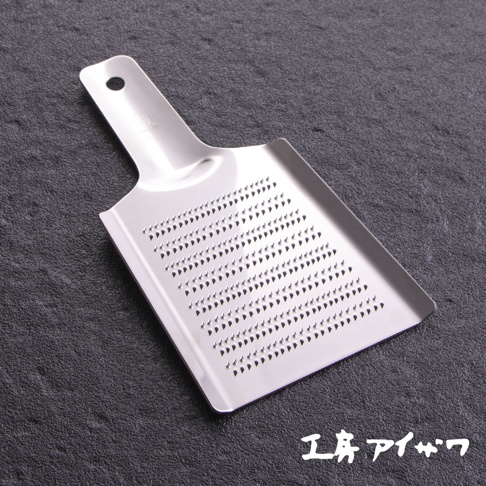 銀色不鏽鋼製成的食材磨泥器，設有手柄和圓孔，磨泥區域佈滿 rows of triangular perforations，用於磨碎食材。