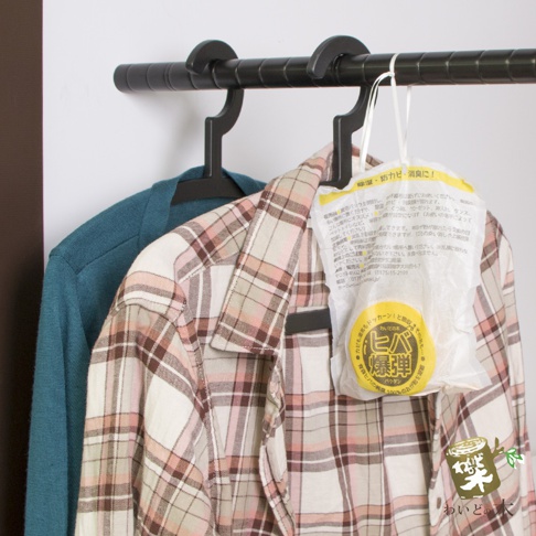 一件藍綠色毛衣掛在一件粉紅色格紋襯衫旁，一件寫有日文的白色包裝產品懸掛在襯衫上。