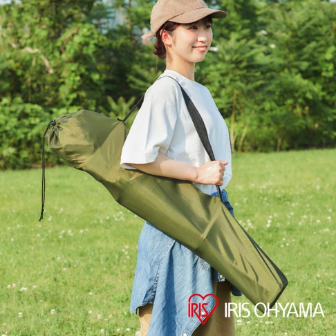 一名女子身穿白色T恤和牛仔裙，斜挎著一個軍綠色摺疊收納袋，袋子裡裝有露營摺疊野餐椅。