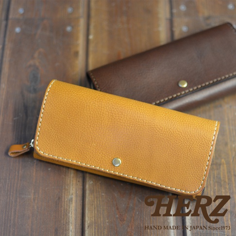 兩款職人手作皮革長夾，一款為淺棕色，另一款為深棕色，皆為寬口設計，附有金屬釦，以白色車線縫製，展現皮革的細緻紋理。