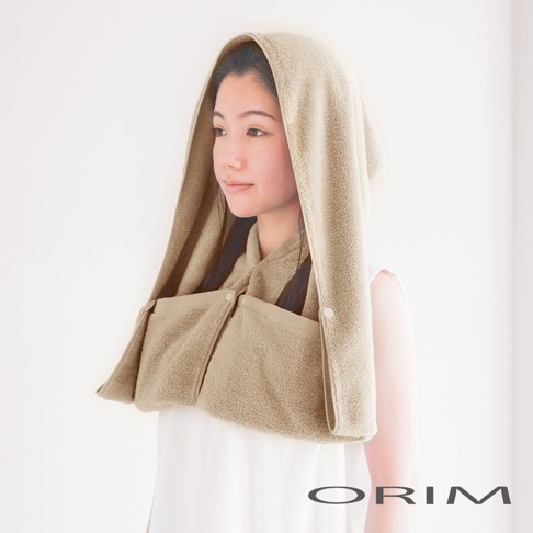 一位女性戴著淺卡其色毛巾材質的吸水頭巾，頭巾有帽子設計，兩側有口袋，並以鈕扣固定。