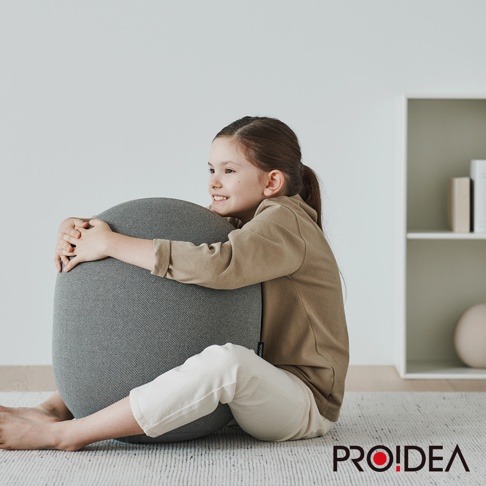 一名小女孩擁抱著一個灰色的針織平衡球，球體呈橢圓形，表面有細密的紋理。