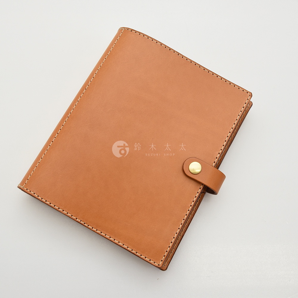 淺棕色皮革A5手帳書套，配有同色系皮革束帶及金色釦子，邊緣縫線清晰。