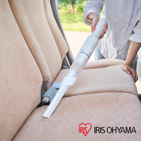 手持無線吸塵器，白色機身，搭配透明集塵筒，用於清潔汽車座椅的織物表面。