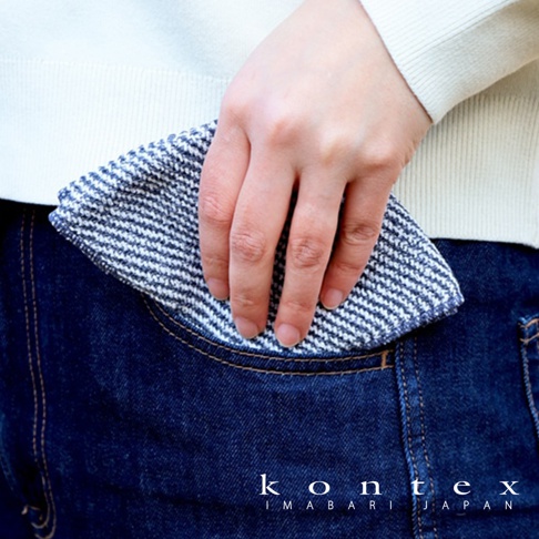 手持藍白條紋的鬆餅紋方巾，方巾材質紋理清晰，輕巧地置於牛仔褲的口袋邊緣。