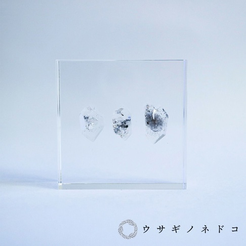 透明壓克力方塊中，三顆帶有銀灰色內含物的天然水晶片狀標本，呈現不規則切面，置於淺藍色背景上。