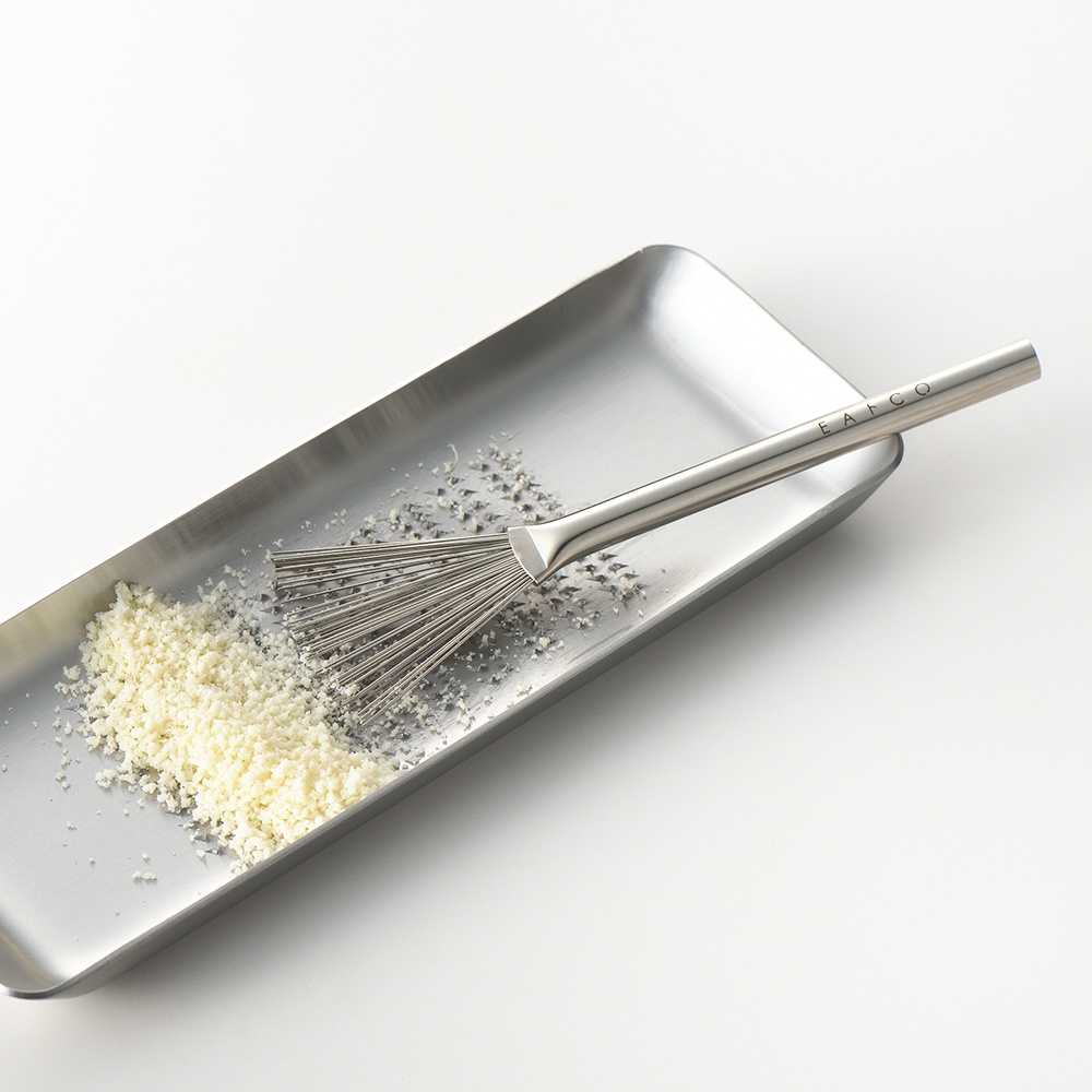 不鏽鋼長方形料理盤內有細緻的白色粉末，盤上放著一支不鏽鋼製的料理小刷，刷頭為細絲狀，手柄上有EATCO字樣。