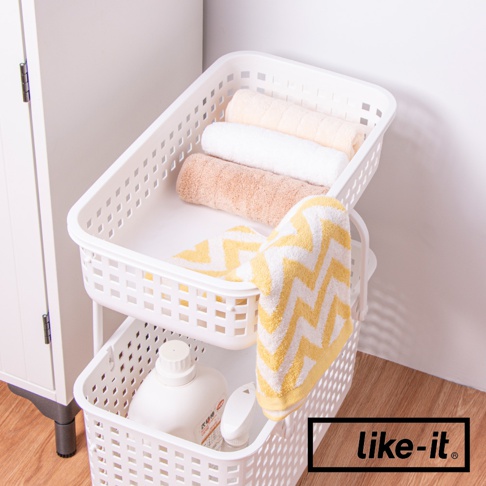 白色塑膠製的兩層洗衣收納籃，上方籃子內有捲起的米色、白色和淺棕色毛巾，下方籃子內有洗衣精瓶和噴霧瓶，籃子側面皆有方形鏤空設計，其中一個籃子掛著一條黃白相間的鋸齒圖案毛巾。