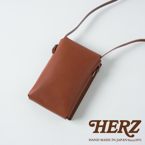 職人手作皮革手機包 CP-11，展現自然的咖啡棕色調。包款採用高品質皮革製作，線條簡潔俐落，配有細長的皮革背帶，適合斜挎或肩背。側面縫線工整，展現細膩的職人手工。