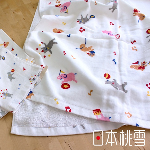 白色紗布毛巾，印有「小小馬戲團」圖案，包括粉紅色大象、灰色兔子、玩著球的猴子等，點綴著音符和星星，材質輕柔。