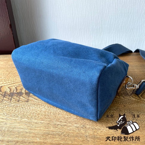 石洗帆布材質的藍色散步包，側面有金屬扣環和皮質裝飾，包包下方有狗與行李箱的圖案，以及日文的「犬印鞄製作所」字樣