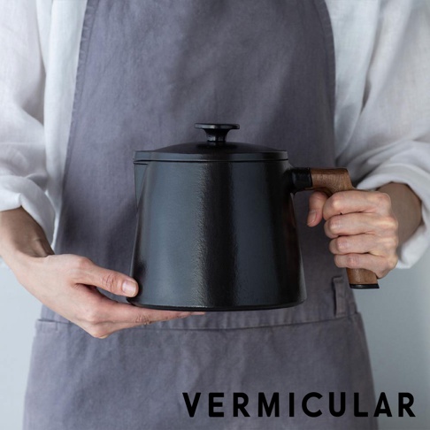 VERMICULAR 琺瑯鑄鐵壺，黑色鑄鐵壺身配木質提把，由雙手捧持，展現品牌標誌。