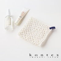 白色棉麻混紡方巾，表面有明顯的鬆餅紋路，一角帶有藍色標籤，旁邊有一支白色噴霧瓶和一條白色軟管。