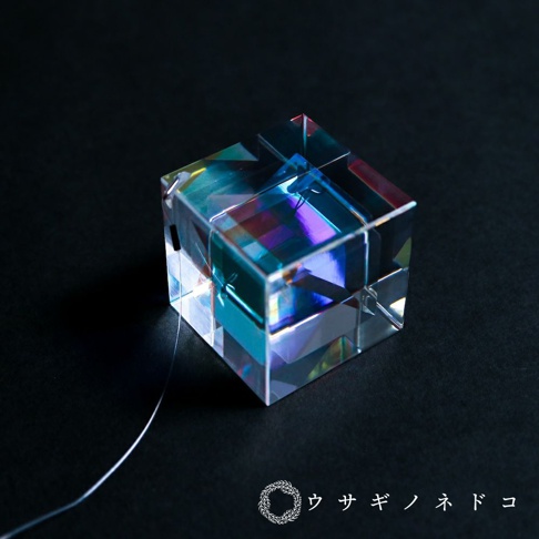 透明玻璃製成的三棱鏡立方體吊飾，表面呈現多種色彩的折射光，如藍色、紫色和粉紅色。