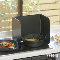 ㄇ型折疊防汙擋油板，黑色金屬材質，兩側擋板向內彎曲，放置於瓦斯爐上，中間有炒菜鍋和油炸鍋。