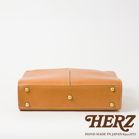 淺棕色皮革雙口袋兩用商務公事包，包身結構簡潔，四角設有金色銅釘，呈現職人手作質感。