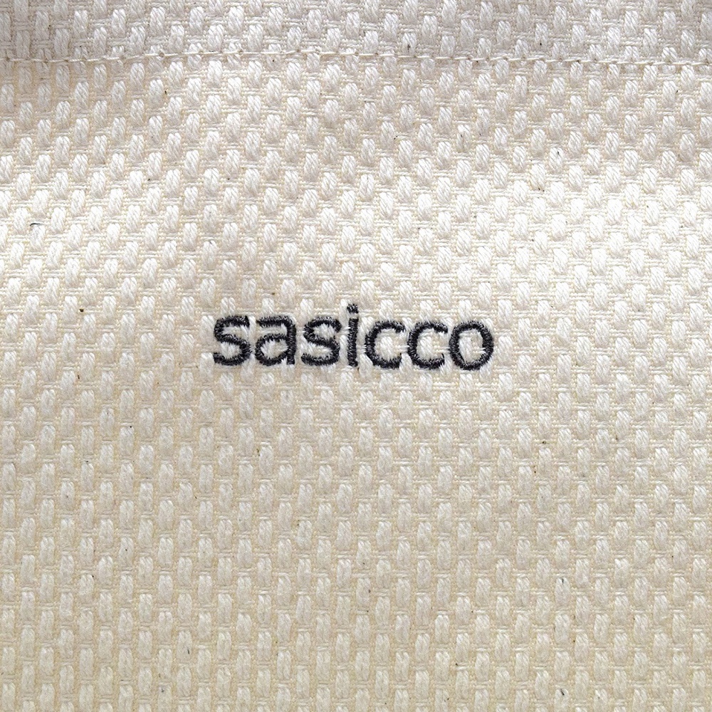 米白色三河木綿刺子織托特包，表面有黑色「sasicco」品牌字樣，織紋細膩，材質紮實。
