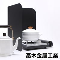 一組黑色的L型折疊擋油板，置於白色背景前，旁邊有一個白色茶壺及一個正在煮食的白色鍋子，鍋子置於一個小型爐具上。