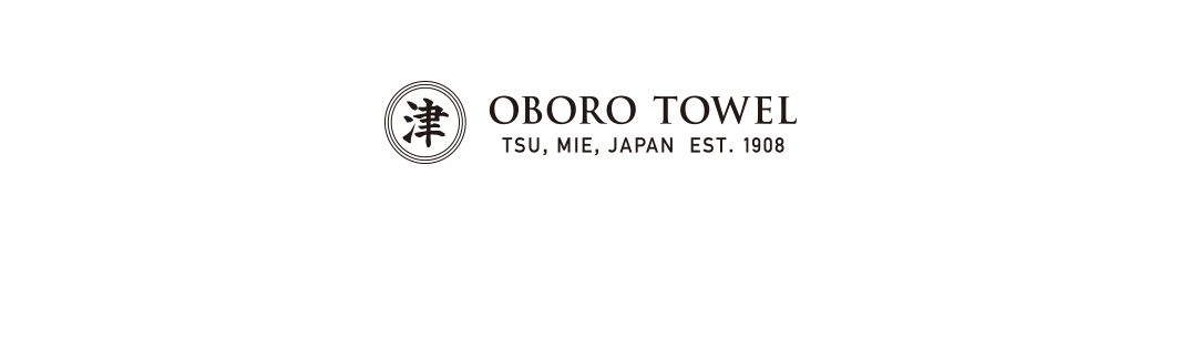 竹棉製成的浴墊和細纖維毛巾禮盒，包含一個圓形標誌，內有日文「津」字，旁邊是 OBORO TOWEL 的品牌名稱，下方註明 TSU, MIE, JAPAN EST. 1908。